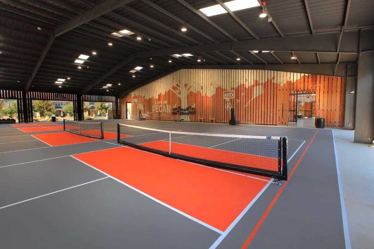 Indoor recreational court with multiple painted playing areas, a high vaulted ceiling with skylights, extensive wood-paneled wall accents, and an open-air architectural design