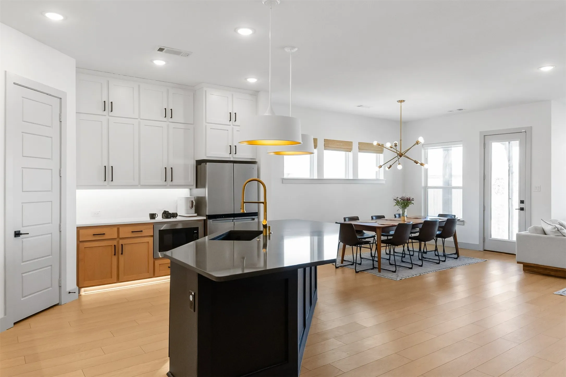 Open-concept kitchen and dining area featuring light wood-finish flooring, a kitchen island with a dark countertop, white upper cabinetry, and a dining area with multiple windows