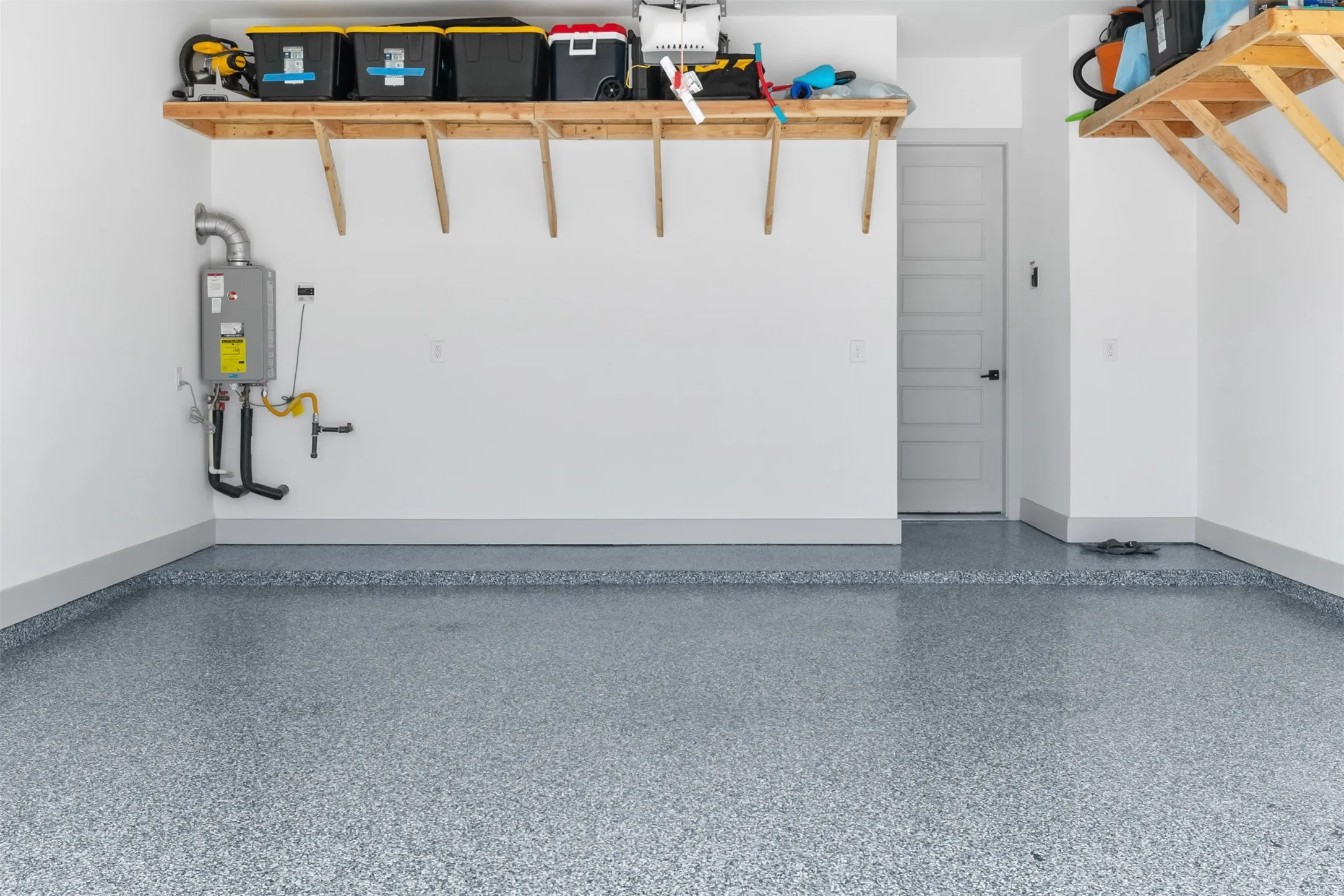 Garage featuring a speckled epoxy floor, built-in wooden shelving, and a tankless water heater