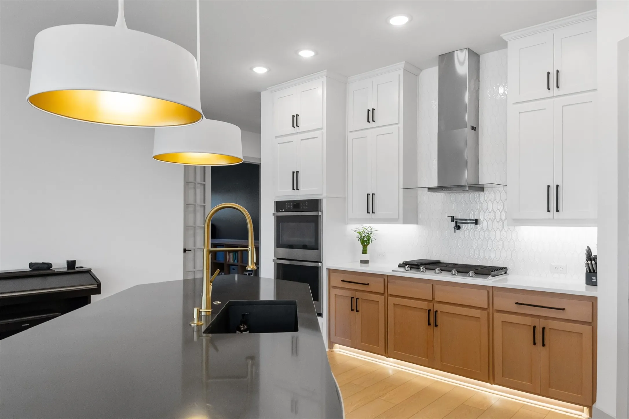 Kitchen featuring a dark countertop island, white and natural wood-tone cabinetry, stainless steel range hood, and pendant lighting