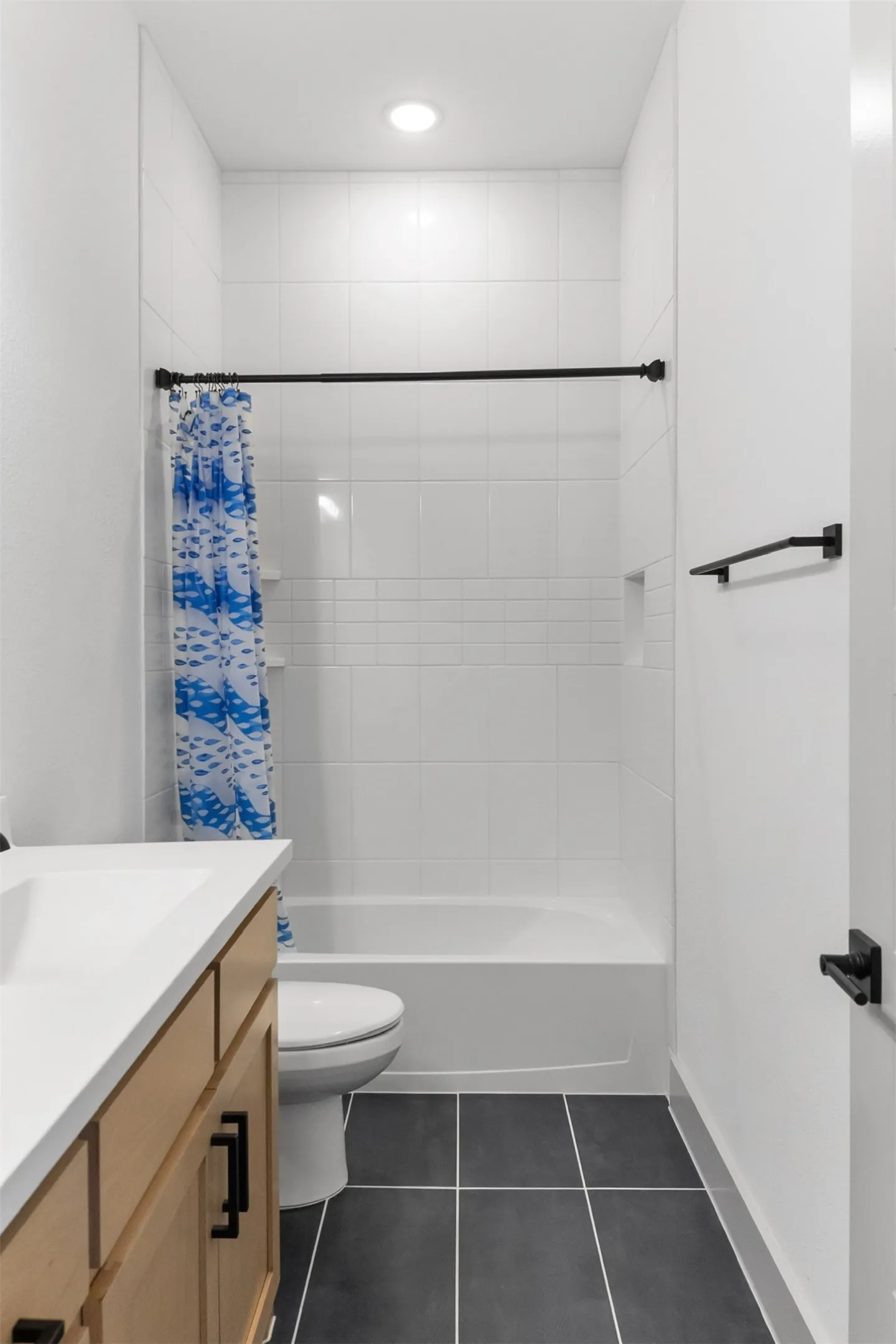 3rd bathroom with built-in bathtub with white tile surround, dark tile flooring, and a light wood-finish vanity with a white countertop