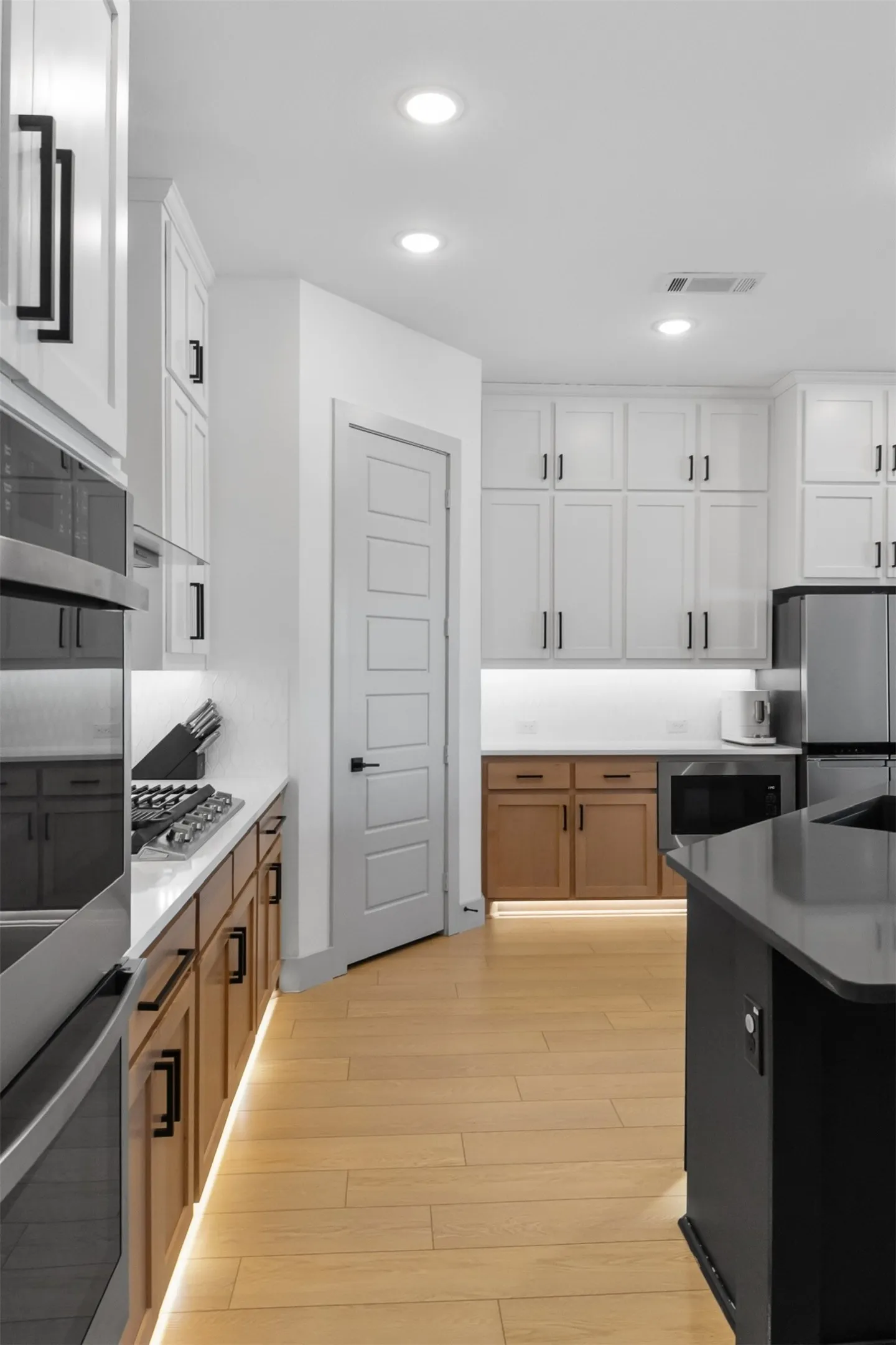 Kitchen featuring light wood-finish flooring, white upper cabinetry, two-tone lower cabinetry, and recessed lighting