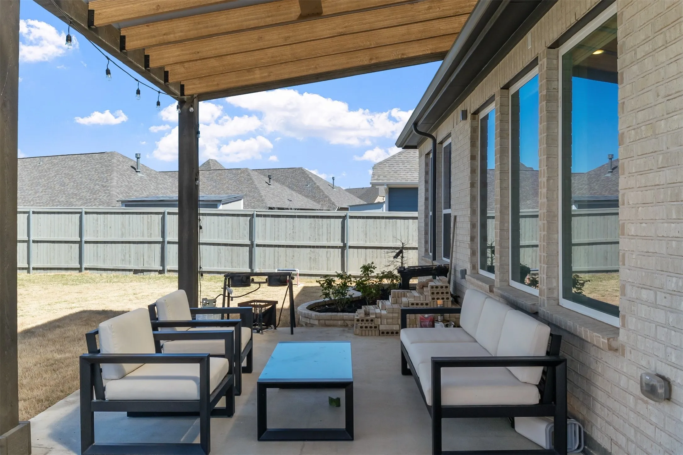 Covered patio with a wood-beam pergola, light-colored brick exterior, and multiple large windows