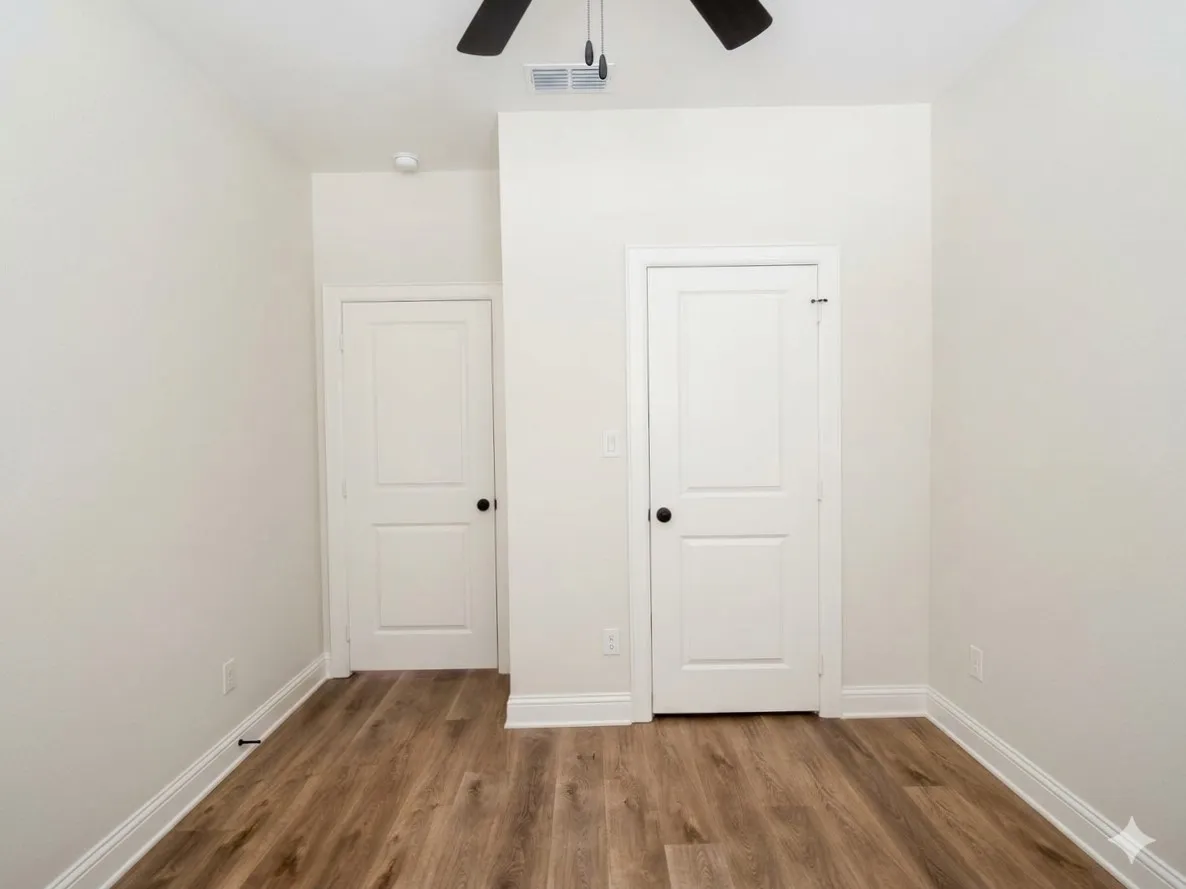 Wood-finish flooring, white paneled doors with black hardware, ceiling fan with black blades, white baseboards, and neutral wall tones
