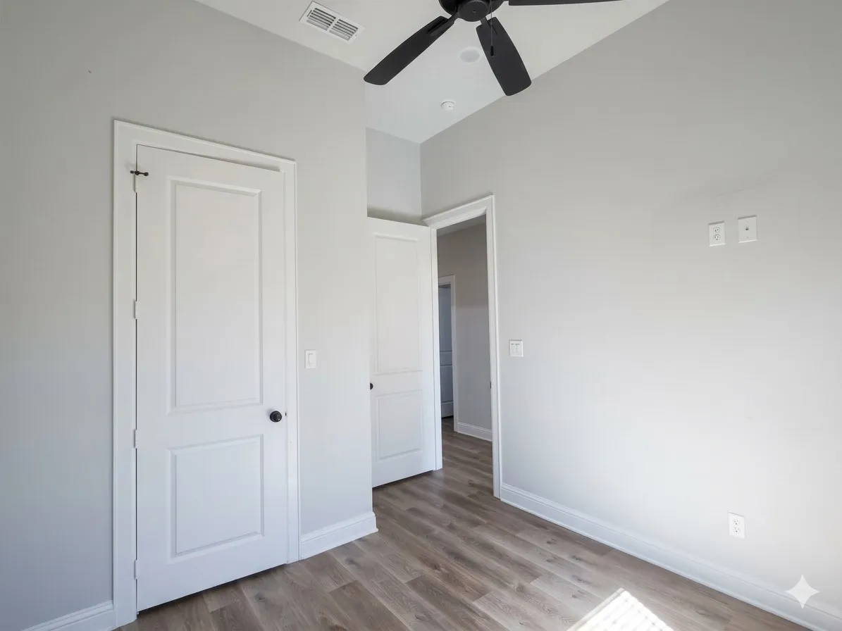 Wood-finish flooring, white panel doors with black hardware, vaulted ceiling, and a ceiling fan