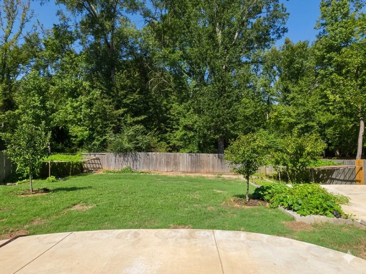 Expansive backyard featuring a concrete patio, a privacy fence, and mature trees