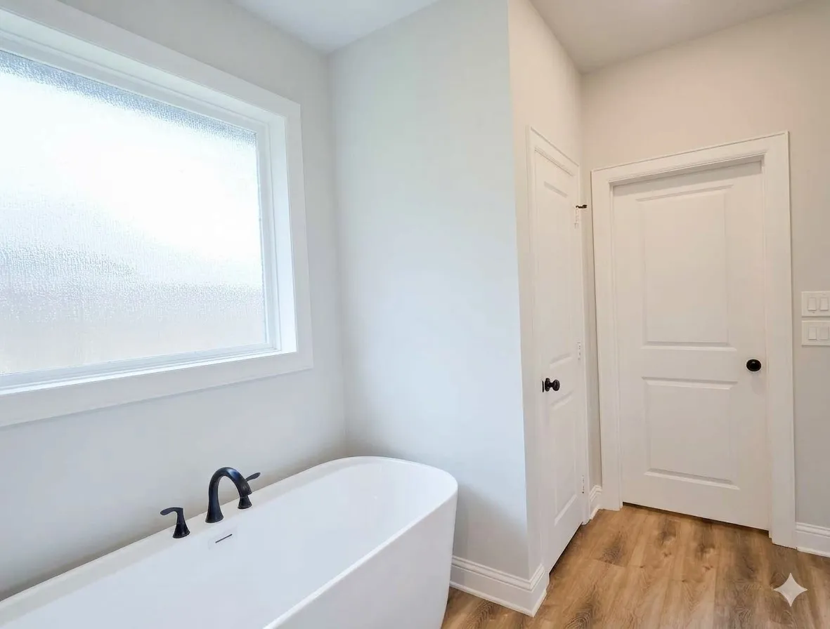 Freestanding soaking tub with matte black fixtures, wood-finish flooring, and a privacy window