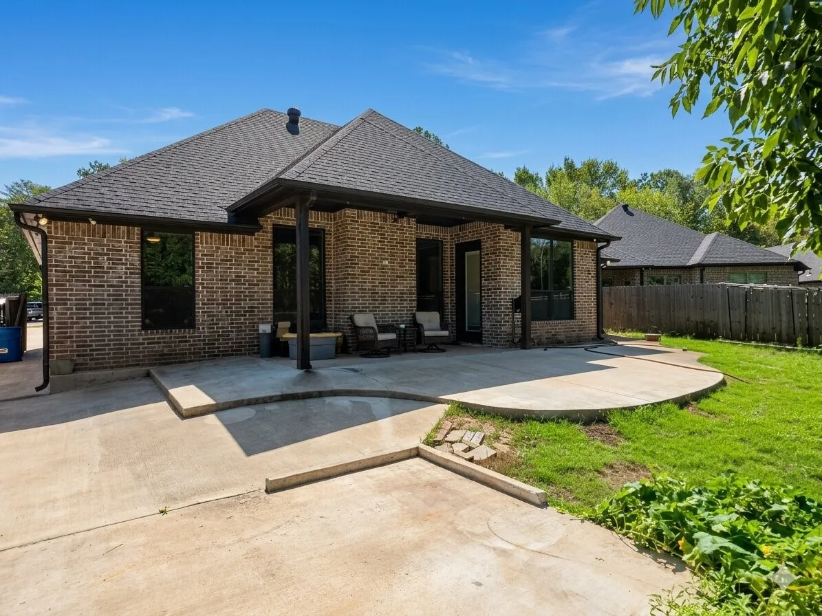 Brick exterior with a covered patio, expansive concrete hardscaping, and a lush lawn