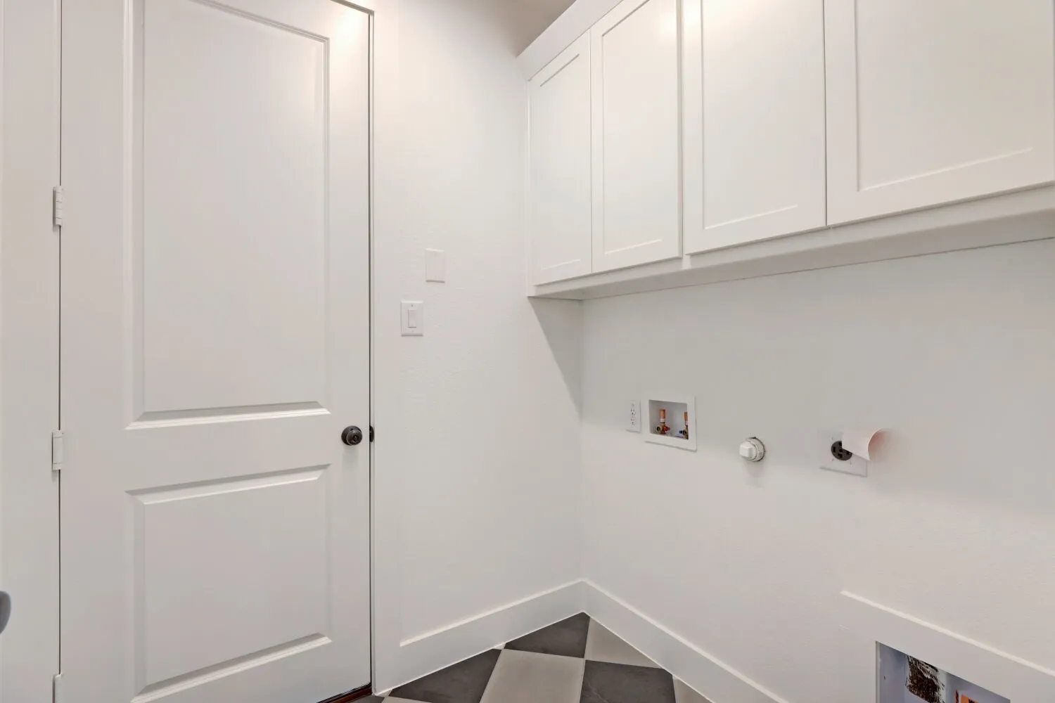 White shaker-style cabinetry, a white paneled door with dark hardware, and checkerboard floor tiling
