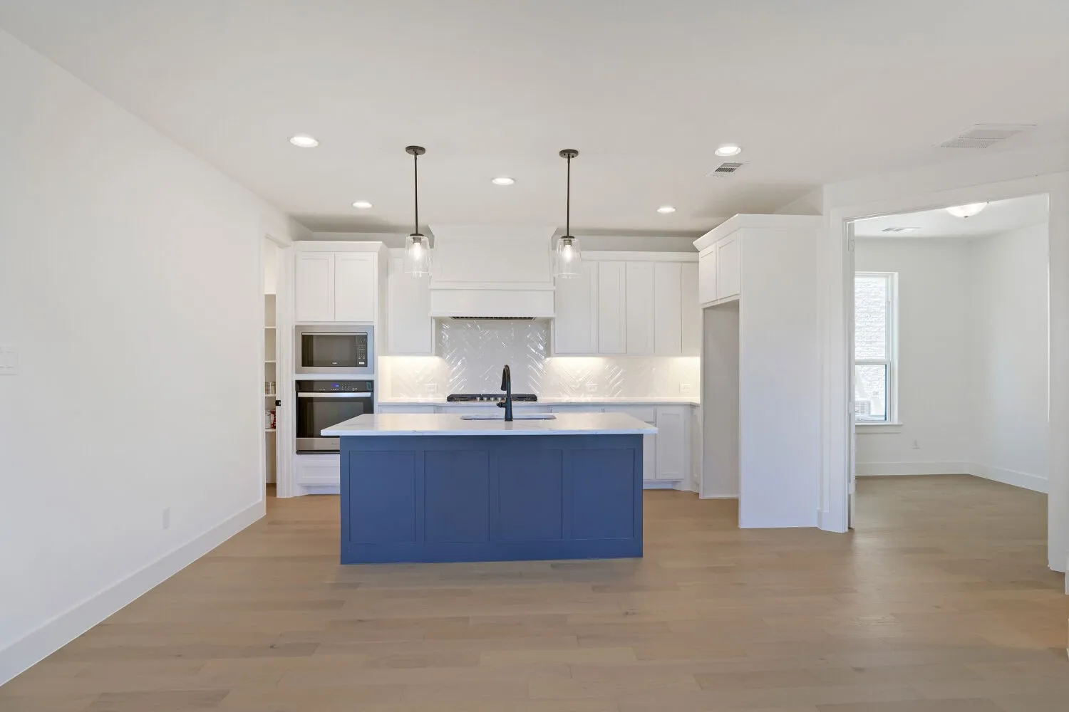 Kitchen featuring a blue island, white cabinetry, integrated double oven, chevron-patterned backsplash, and wood-finish flooring