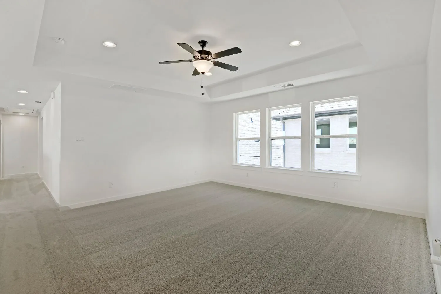Spacious room featuring a tray ceiling with a ceiling fan, recessed lighting, three large windows, and neutral carpeting