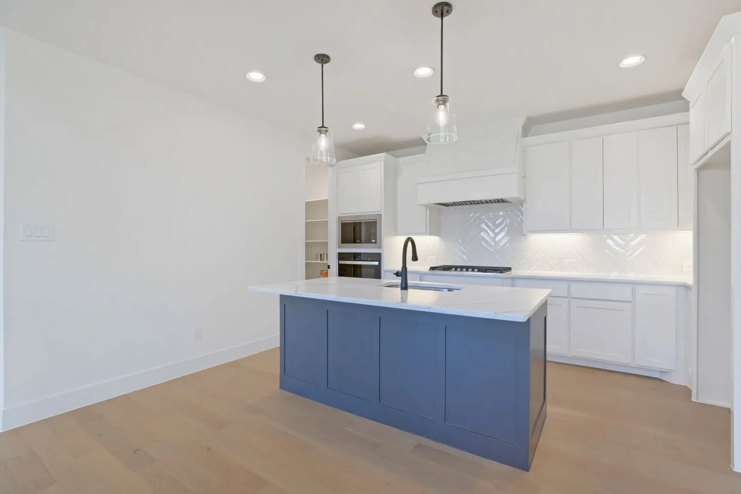 Kitchen featuring a blue island with a white countertop, white cabinetry, integrated appliances, chevron pattern backsplash, and wood-finish flooring