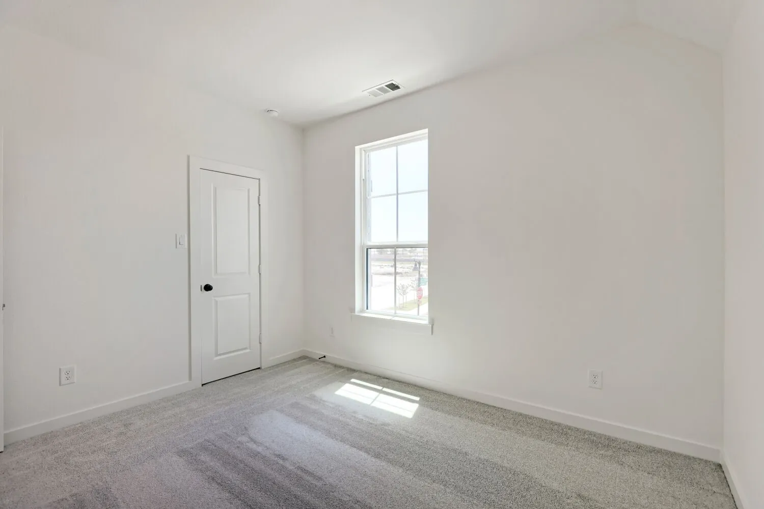 Recessed lighting, sloped ceiling, light gray carpeting, paneled interior door with dark hardware, and a window with white trim