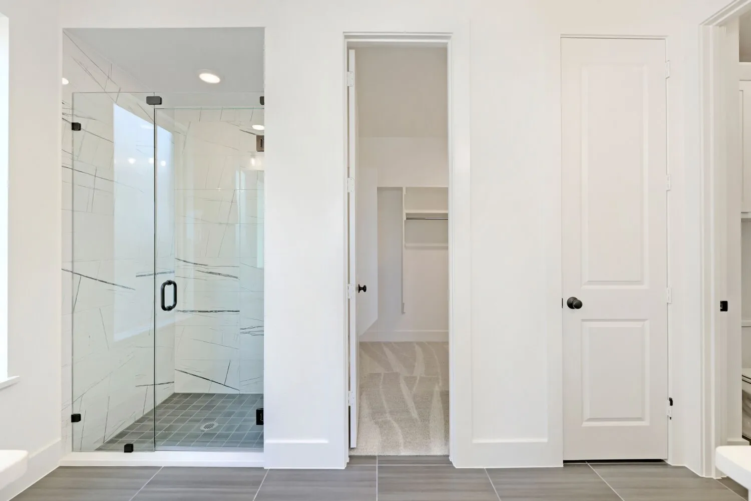 Walk-in shower with clear glass enclosure and black hardware, patterned tile shower surround, gray tile flooring, recessed lighting, and a separate closet space with shelving