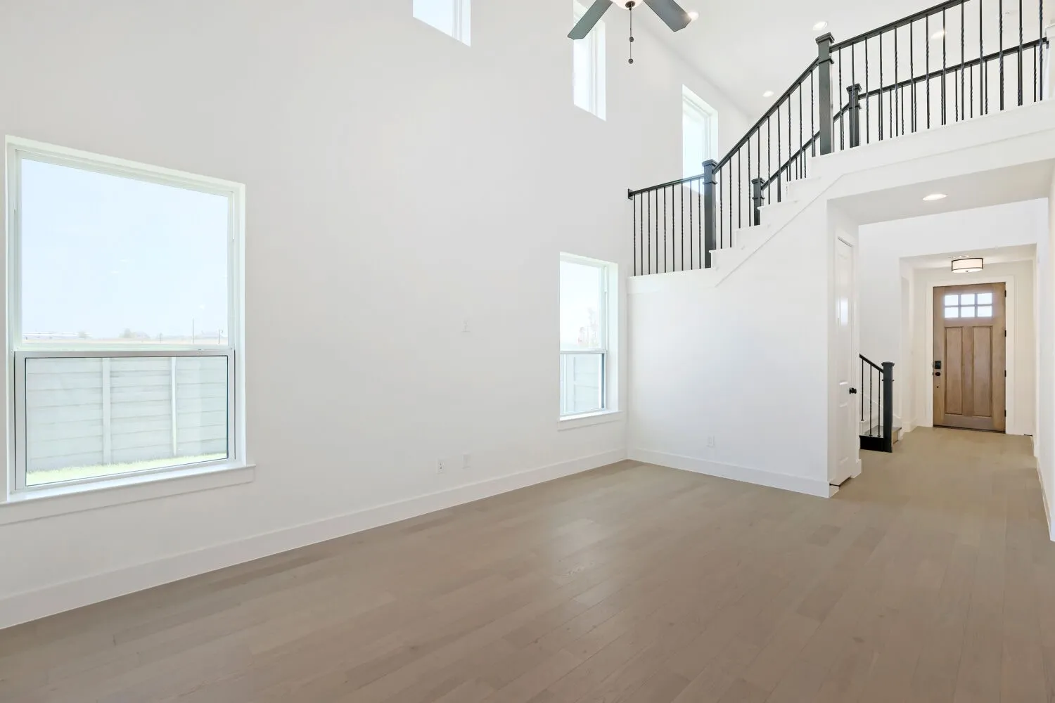 Two-story living area featuring wood-finish flooring, a contemporary ceiling fan, and multiple windows