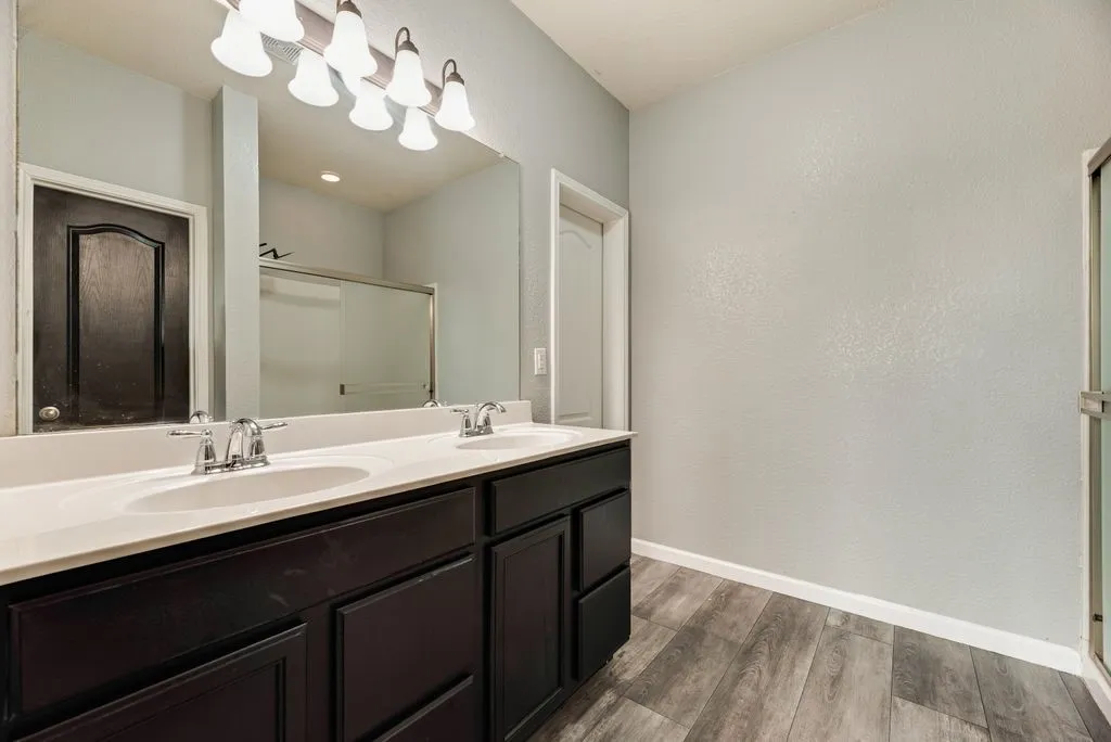 Dual-vanity bathroom featuring a long white quartz countertop, dark cabinetry with multiple drawers, polished chrome faucets, an expansive framed mirror, and contemporary wall-mounted lighting fixtures