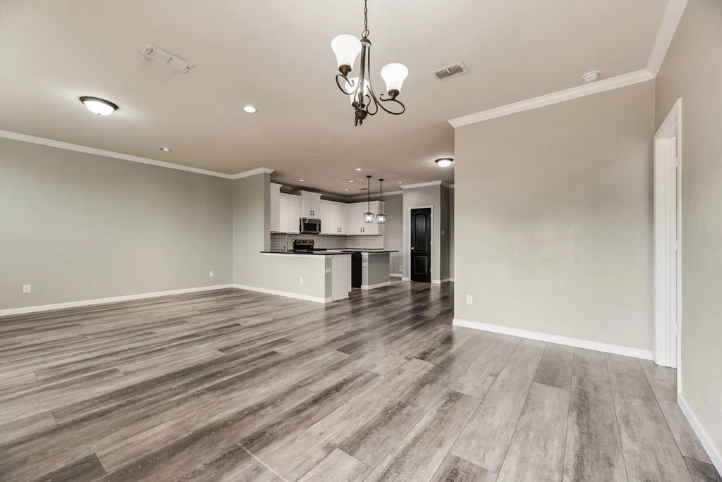 Spacious open-concept living area with wood-finish flooring throughout, recessed ceiling lighting, and a decorative pendant fixture