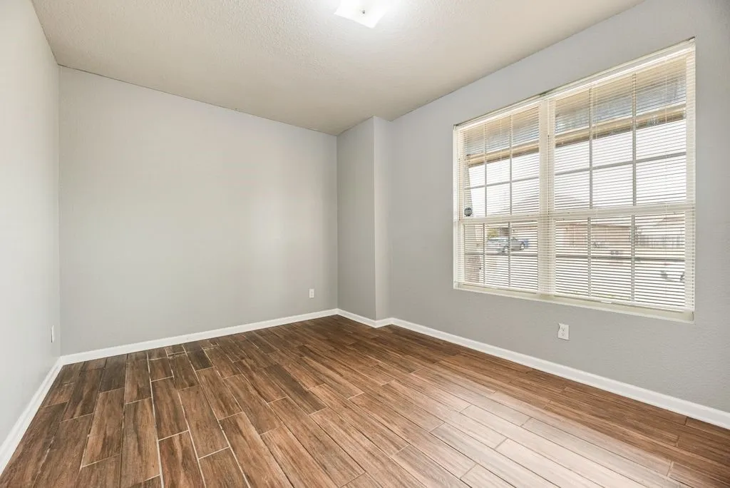 Bright, light-filled bedroom featuring gleaming wood-finish flooring, neutral wall finishes, and expansive gridded windows with interior shutters providing natural illumination and privacy control