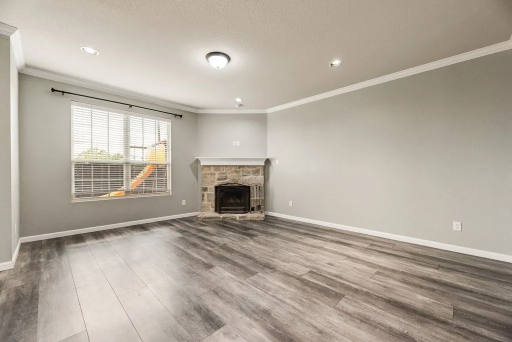 Spacious living room showcasing wood-finish flooring, recessed ceiling lighting, and large windows with plantation shutters