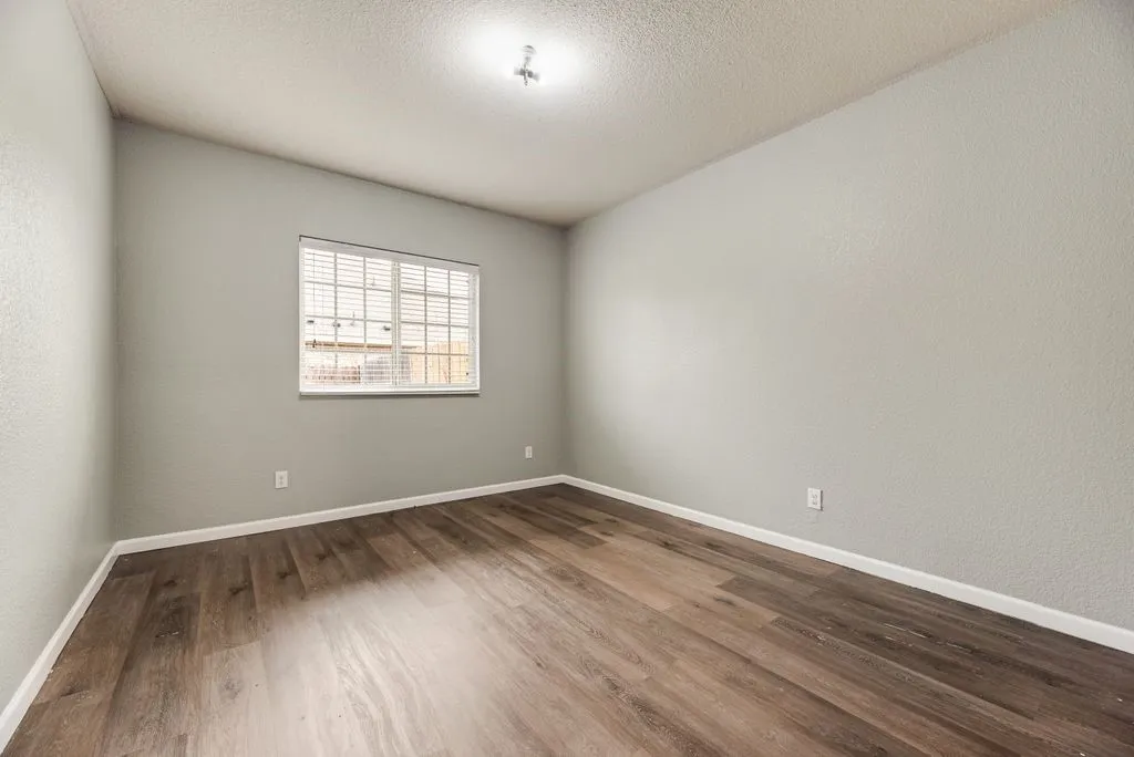 Bright, neutral bedroom featuring wood-finish flooring, recessed ceiling lighting, and large window with security bars providing natural illumination