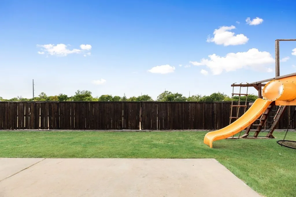 Expansive backyard featuring a manicured lawn, a full-height privacy fence, and a concrete patio