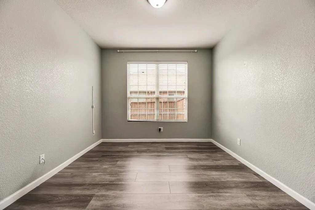 Wood-finish flooring, textured walls, window with horizontal blinds, and a flush mount ceiling light fixture