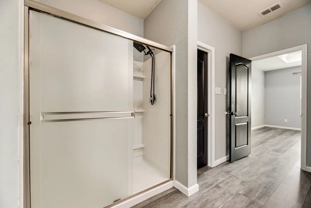 Primary bathroom featuring a frameless glass-enclosed walk-in shower with chrome fixtures, white subway tile surround, and polished wood-finish flooring