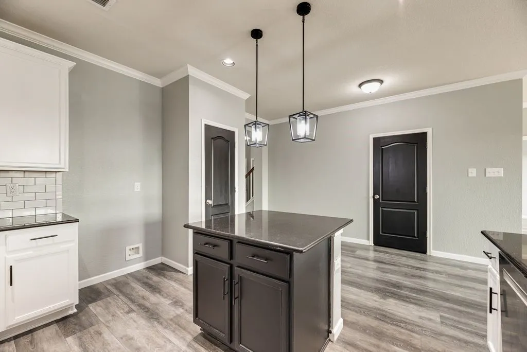 Modern kitchen and dining area featuring a dark-stained island with storage cabinetry, wood-finish flooring throughout, and pendant lighting with glass shades