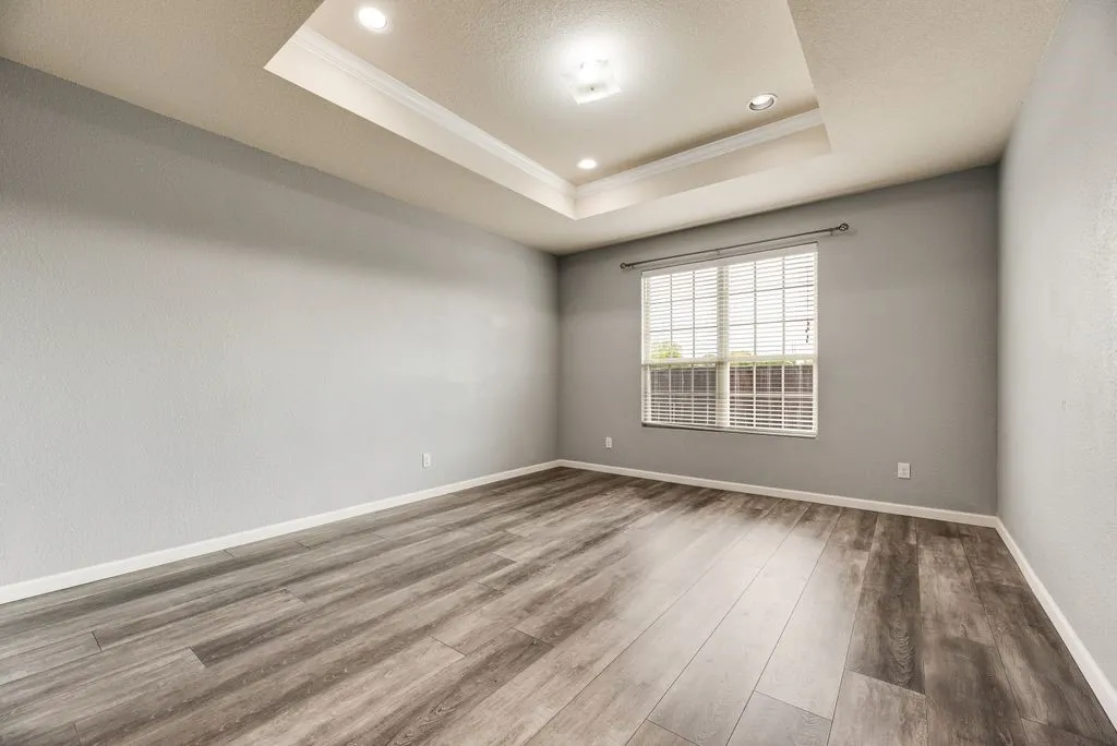 Spacious room featuring wood-finish flooring, recessed ceiling lighting with architectural detail, large window with grid-pattern glazing providing natural light, and neutral wall finishes throughout