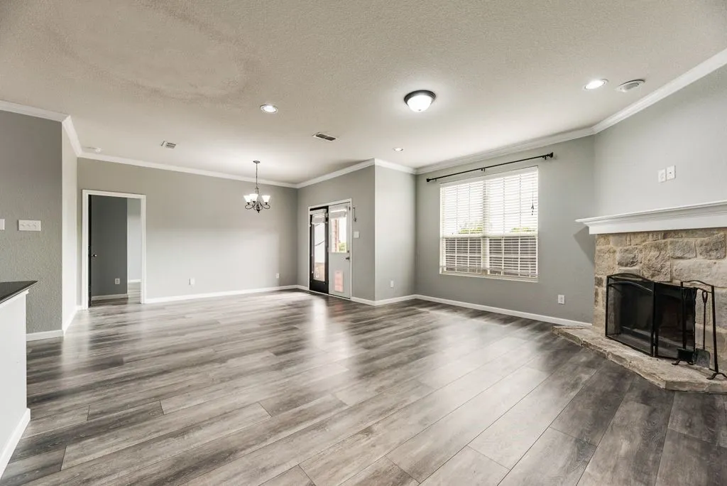 Wood-finish flooring, stone-surround fireplace, recessed lighting, crown molding, and a chandelier fixture