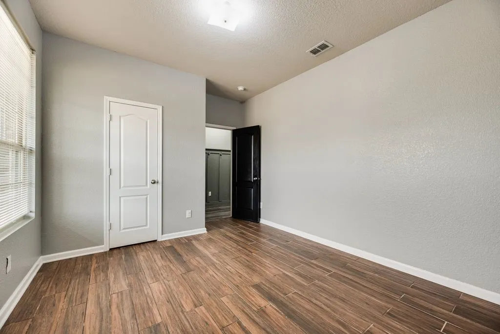 Bright, spacious bedroom featuring warm wood-finish flooring, clean white six-panel closet door, and recessed ceiling lighting