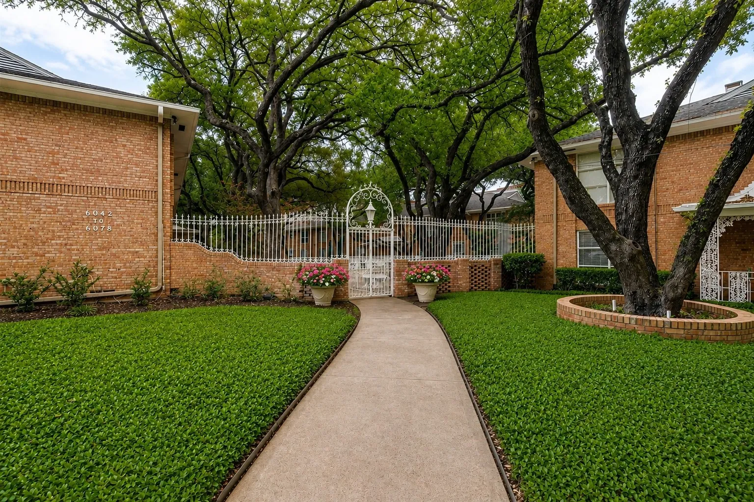 CHARMING COURTYARD ENTRANCE: A winding walkway leads through beautifully maintained grounds beneath a canopy of mature trees to the gated courtyard, creating a welcoming and peaceful setting for 6040 Place, a Preston Hollow Community.