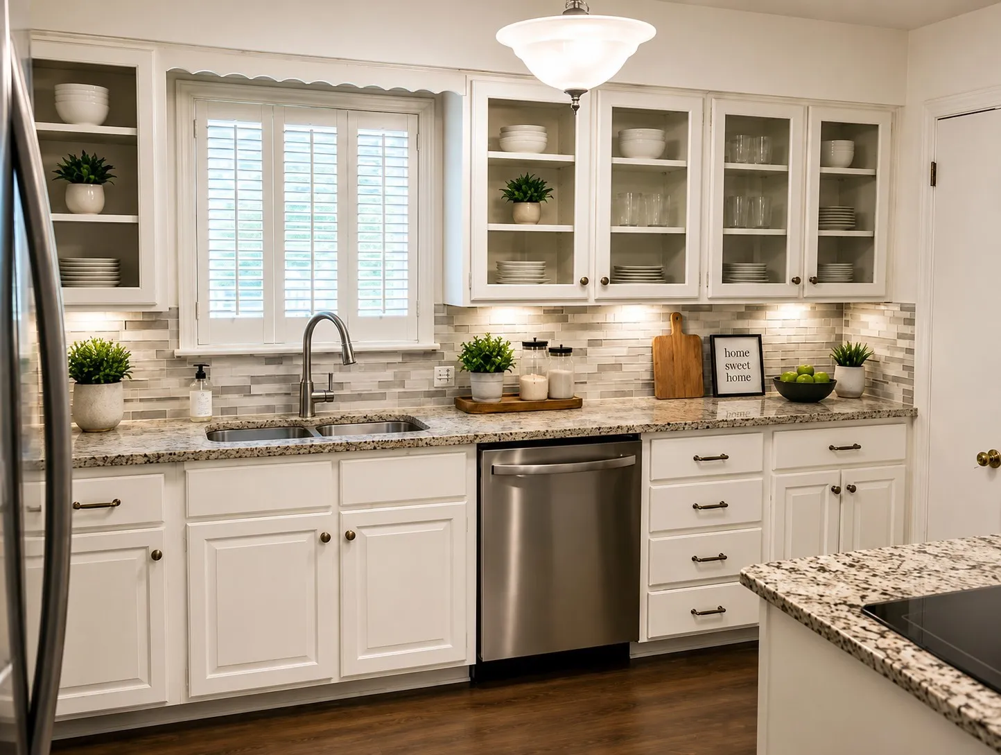 LIGHT & BRIGHT KITCHEN: Crisp white cabinetry, glass-front display cabinets, granite countertops and stainless-steel appliances create a fresh, inviting space. Plantation shutters over the sink, under-cabinet lighting and abundant storage add both charm and functionality. Virtually staged.