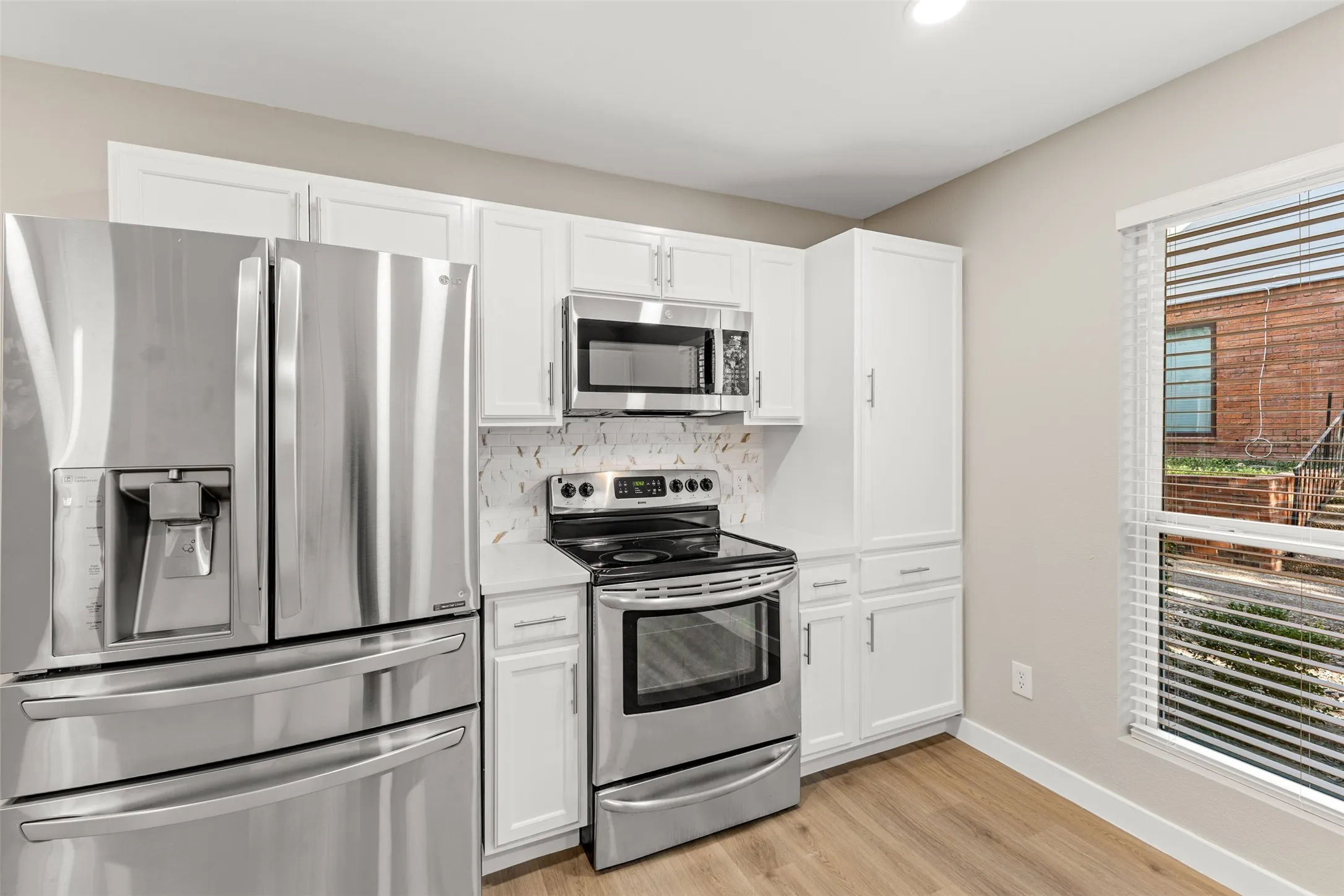 Kitchen featuring stainless steel appliances, white cabinetry, a tiled backsplash, and wood-finish flooring