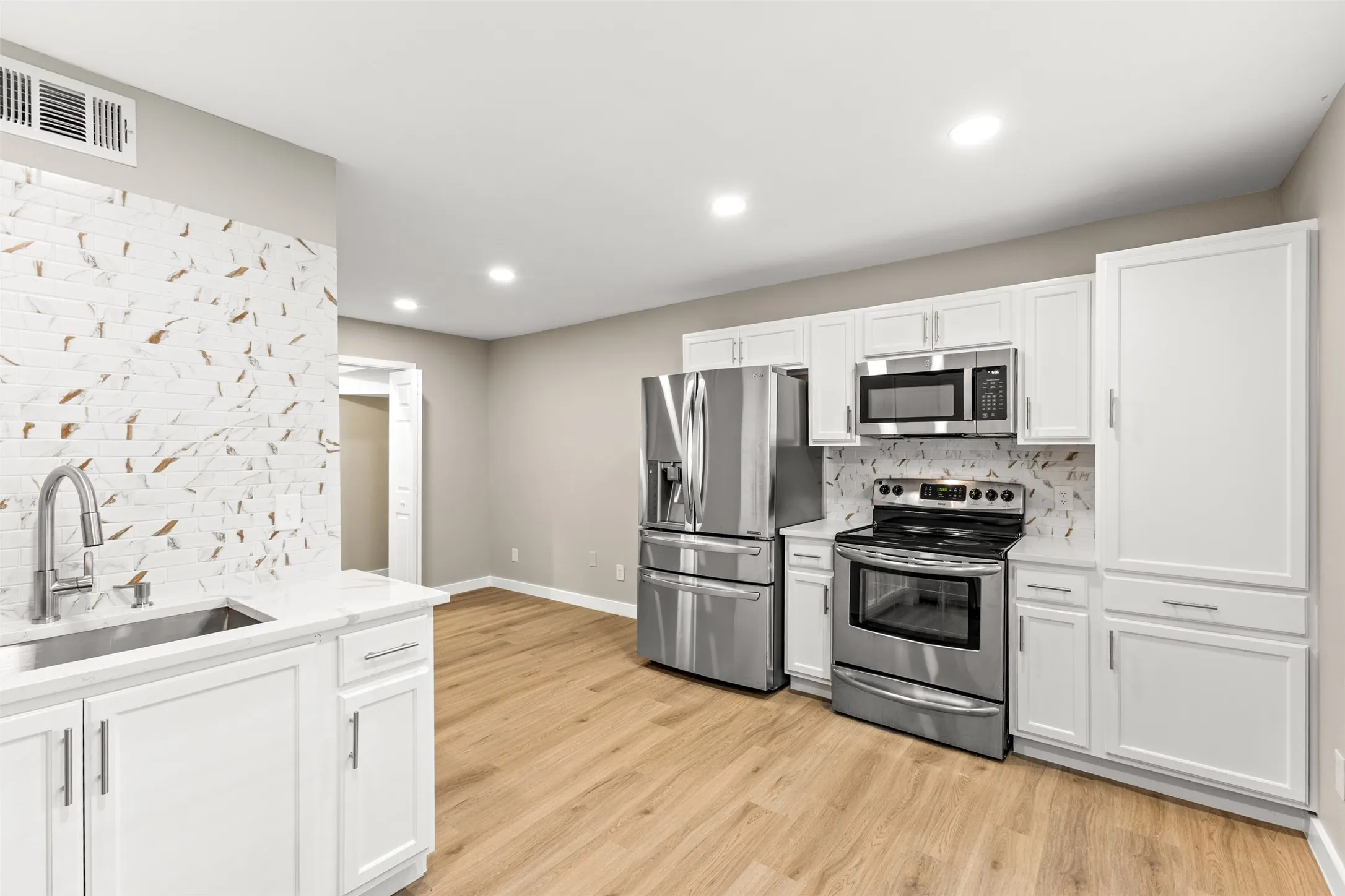Contemporary kitchen featuring stainless steel appliances, white cabinetry, a tiled backsplash, wood-finish flooring, and recessed lighting