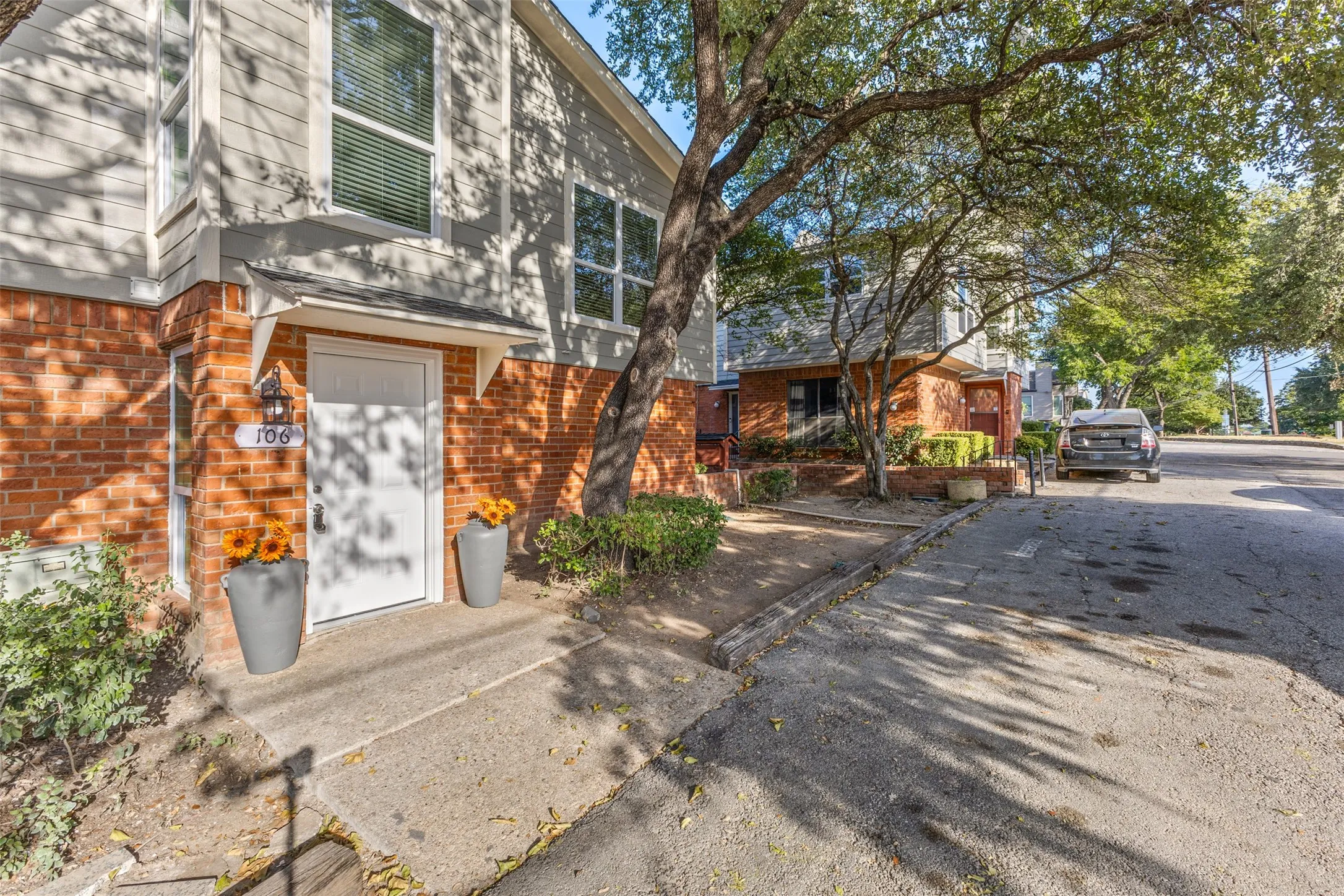 Brick and siding exterior, white entry door with overhead awning, concrete walkway, and mature trees