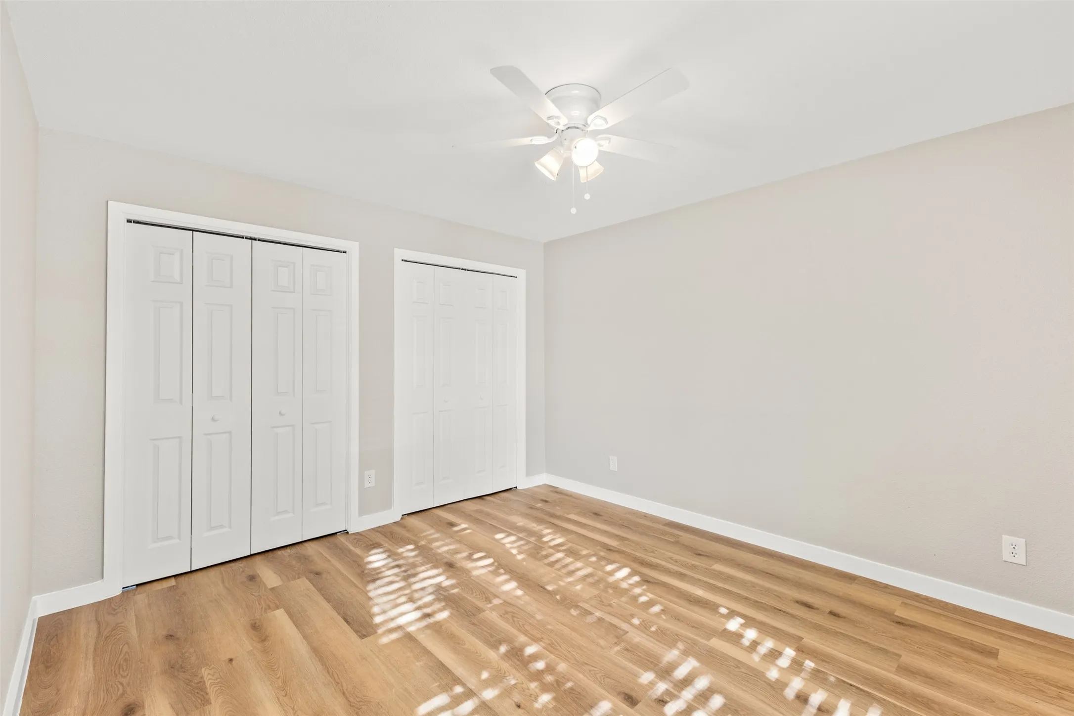 Light wood-finish flooring, two sets of bi-fold closet doors, ceiling fan with integrated lighting, and neutral wall tones