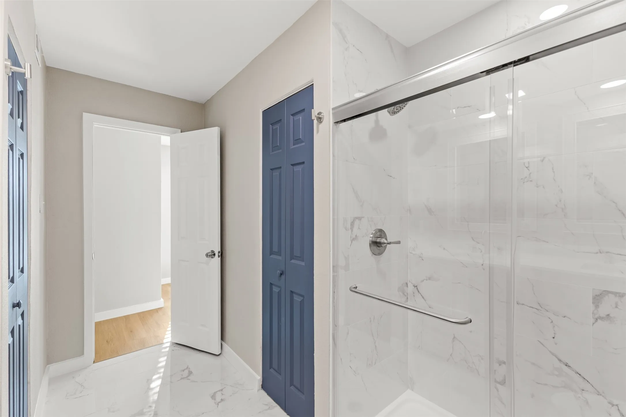Large glass-enclosed shower with white marble-look wall tiles, chrome fixtures, and a bi-fold closet door
