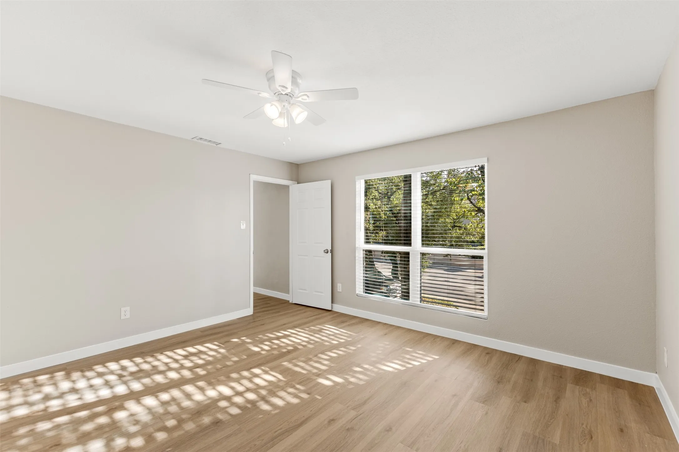 Expansive room featuring wood-finish flooring, a large window with blinds, and an overhead ceiling fan