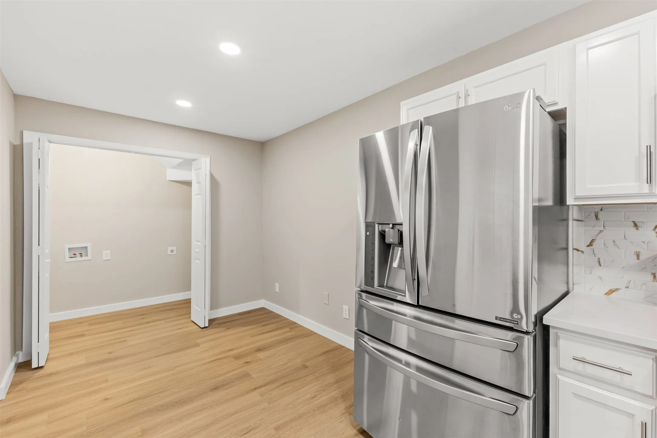 Recessed lighting, wood-finish flooring, white cabinetry, integrated stainless steel refrigerator, and tiled backsplash