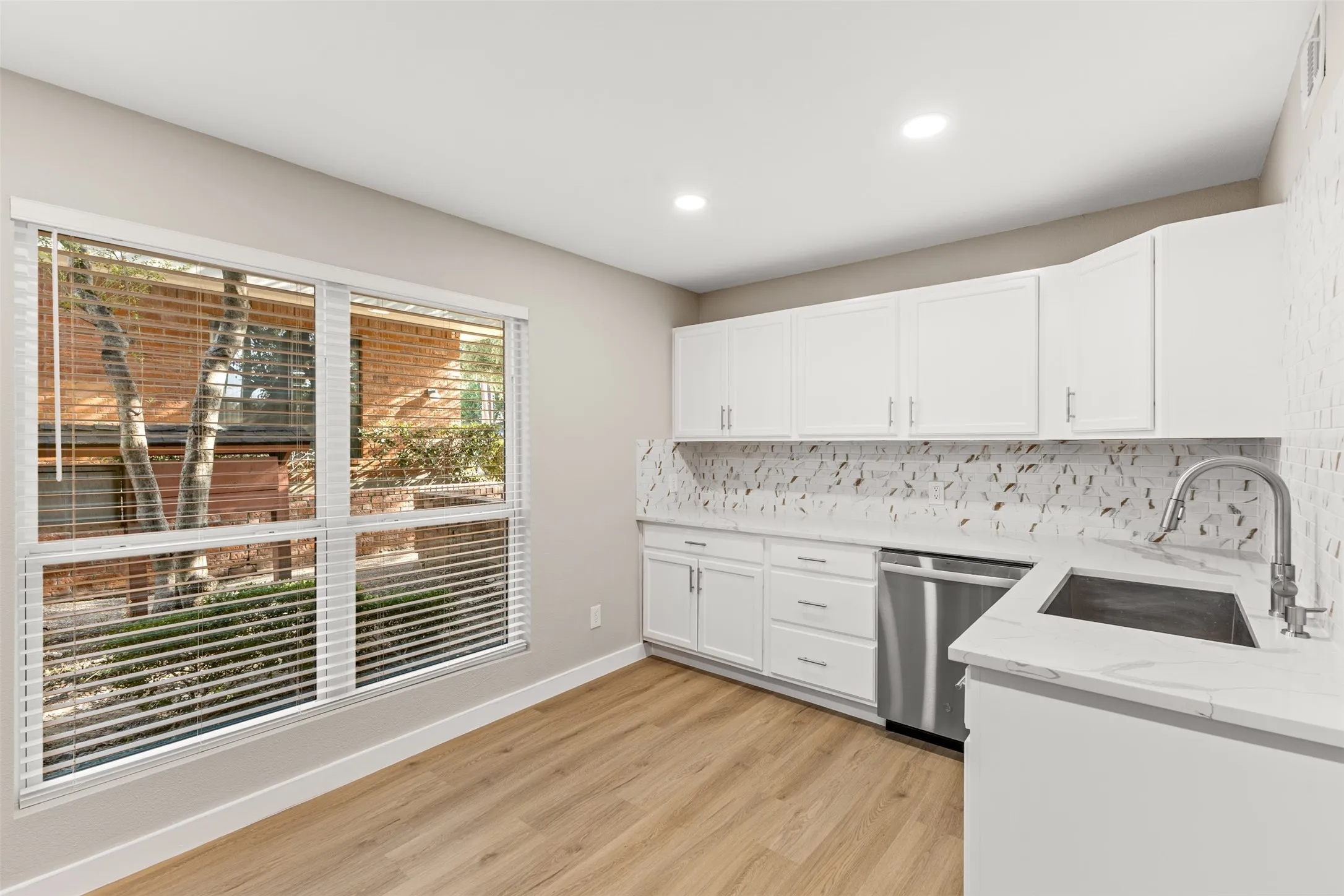 White cabinetry with brushed nickel hardware, stainless steel sink, patterned tile backsplash, wood-finish flooring, and recessed lighting