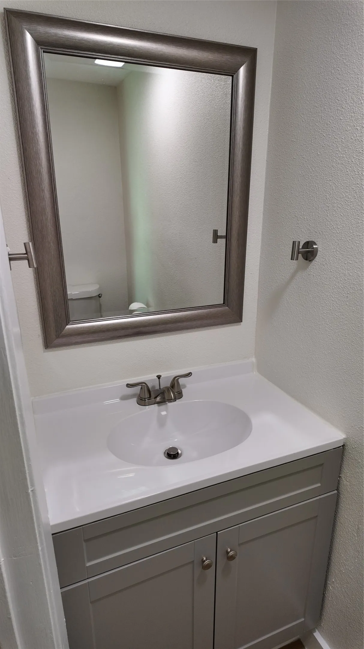 Single vanity with a framed mirror, gray shaker-style cabinetry, an integrated white sink, and brushed nickel hardware