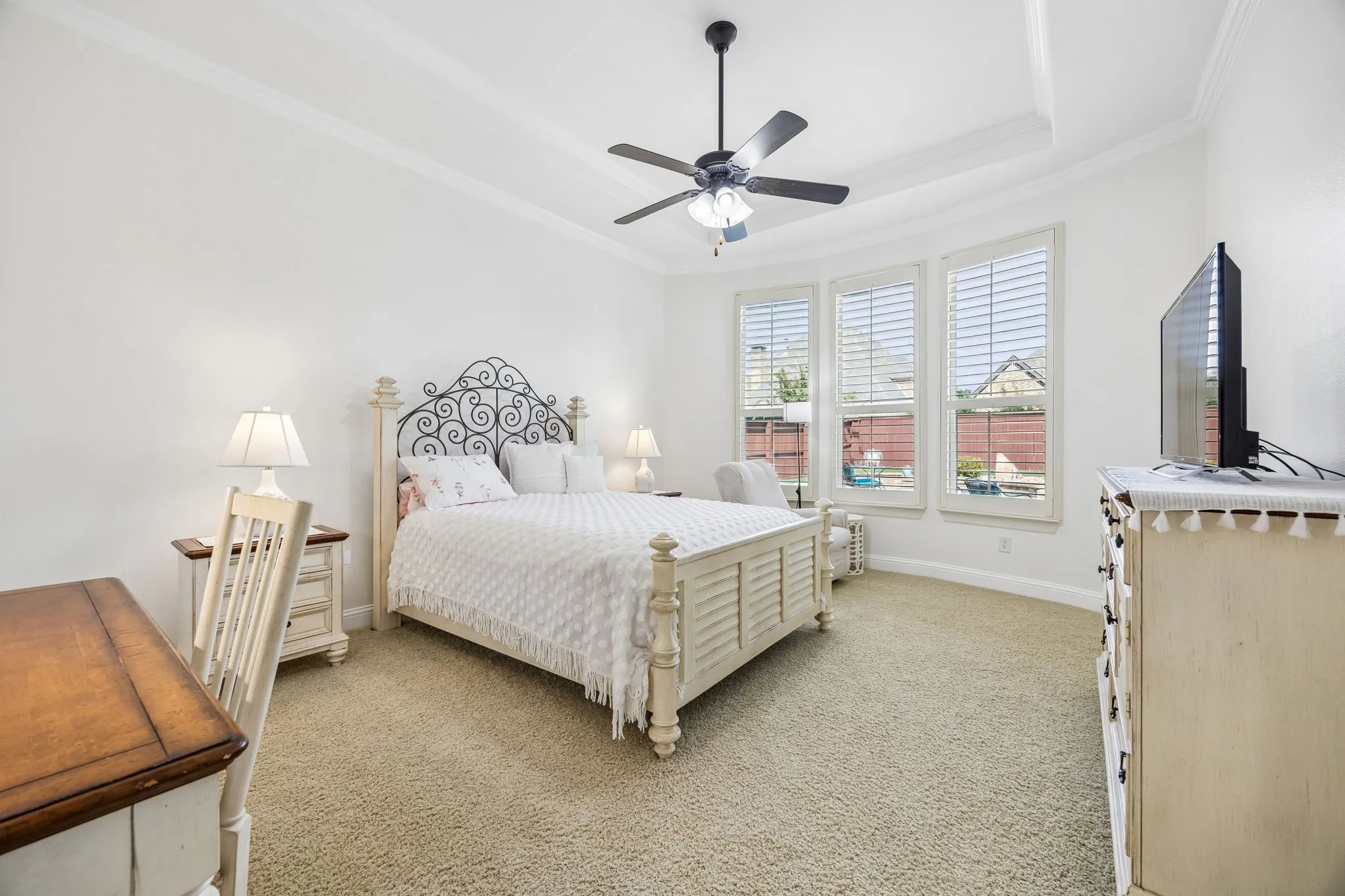 Primary bedroom is large enough for a sitting area by the windows.  Shutters, ceiling fan, carpet, and a tray ceiling.  Ensuite bathroom and walk in closet.
