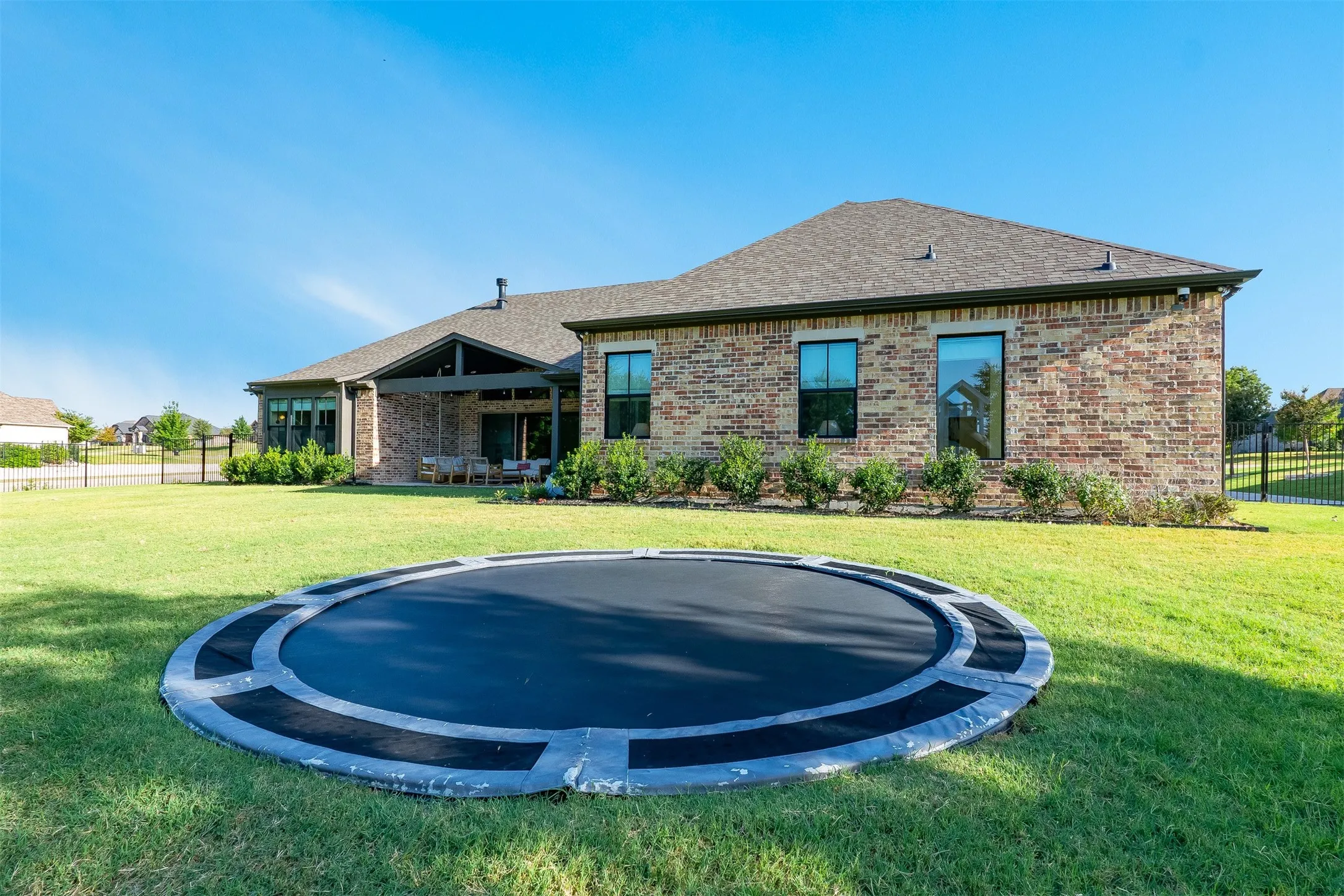 Expansive rear lawn, covered patio, brick and stone exterior, dark-framed windows, and mature perimeter landscaping