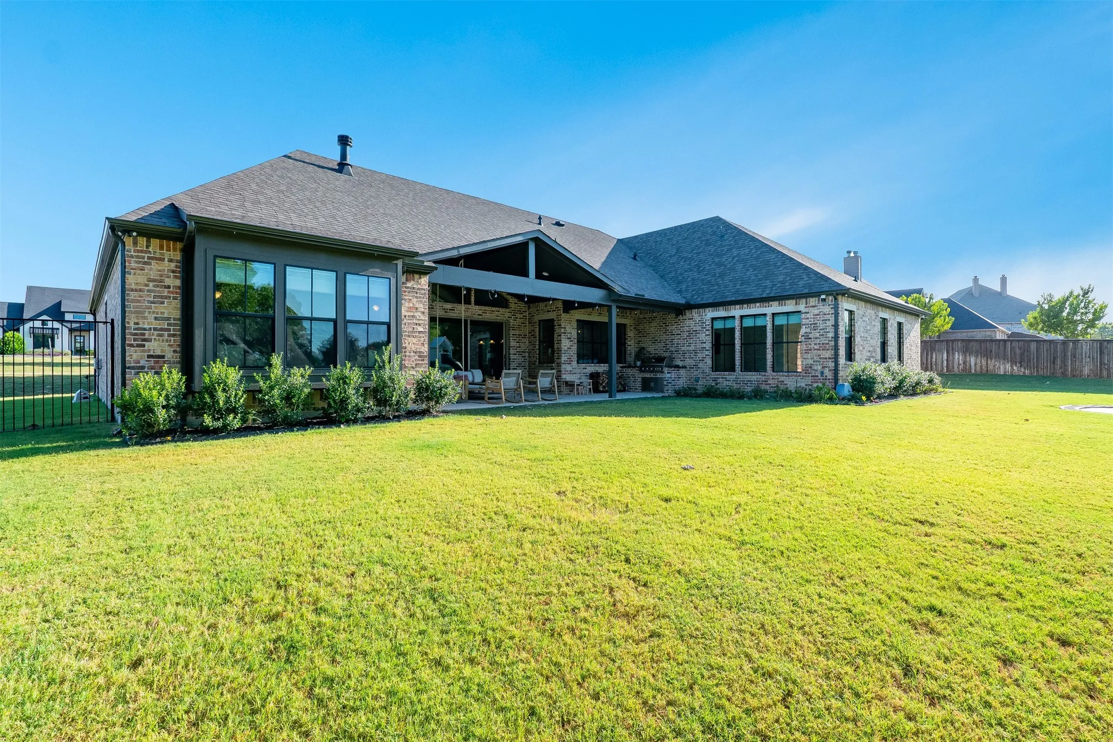 Expansive backyard featuring a manicured lawn, brick exterior, multiple large windows, and a covered patio area