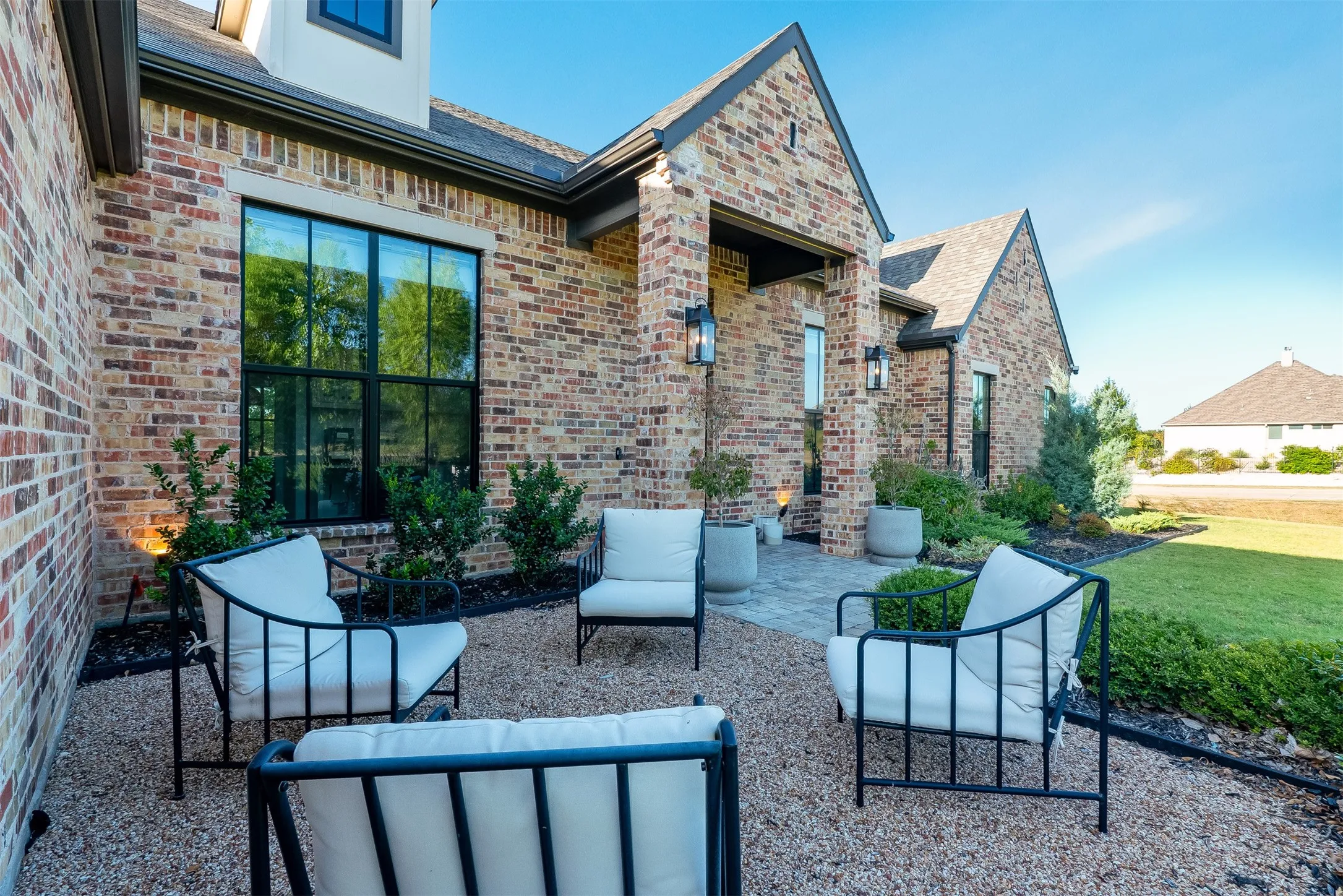 Brick exterior with black-framed windows, gabled roofline, paver patio, and pea gravel landscaping
