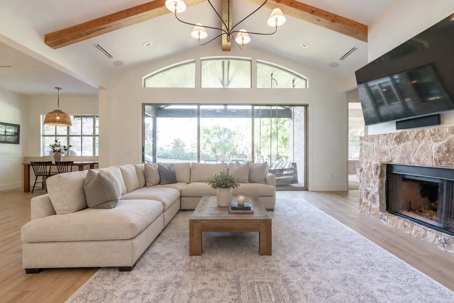 Vaulted ceiling with exposed wood beams, stone-clad fireplace, large sliding glass doors, and wood-finish flooring