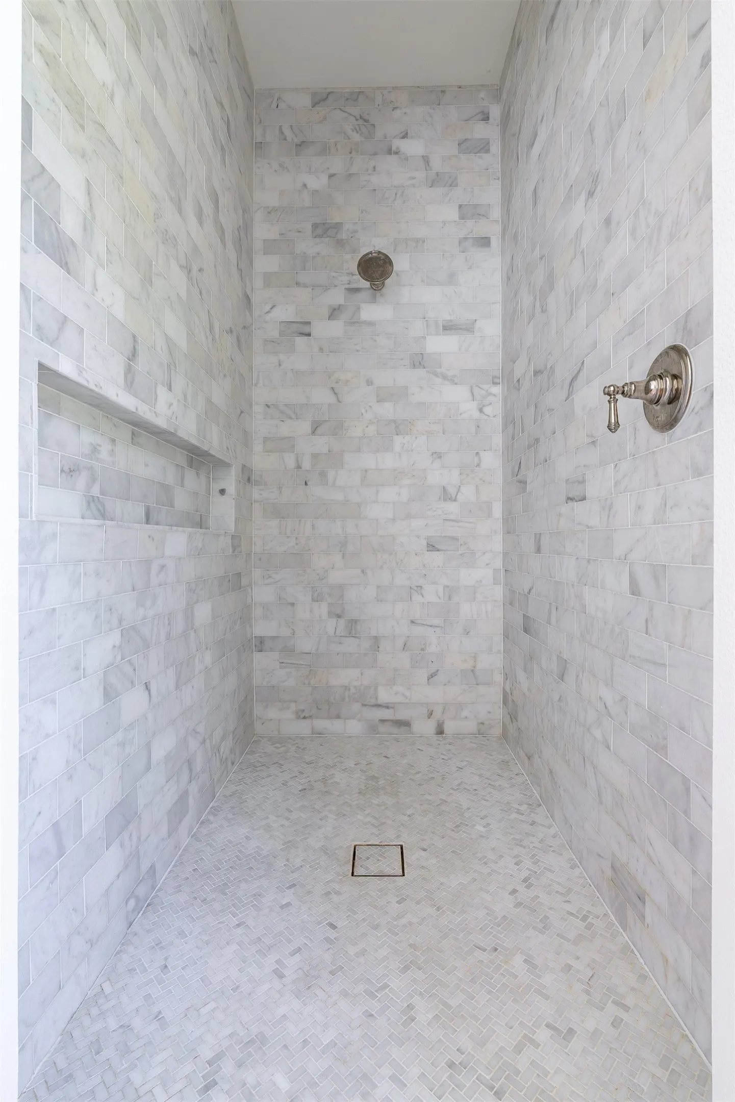 Shower enclosure featuring full-height light-toned tile, a built-in shower niche, and a herringbone-patterned tile floor