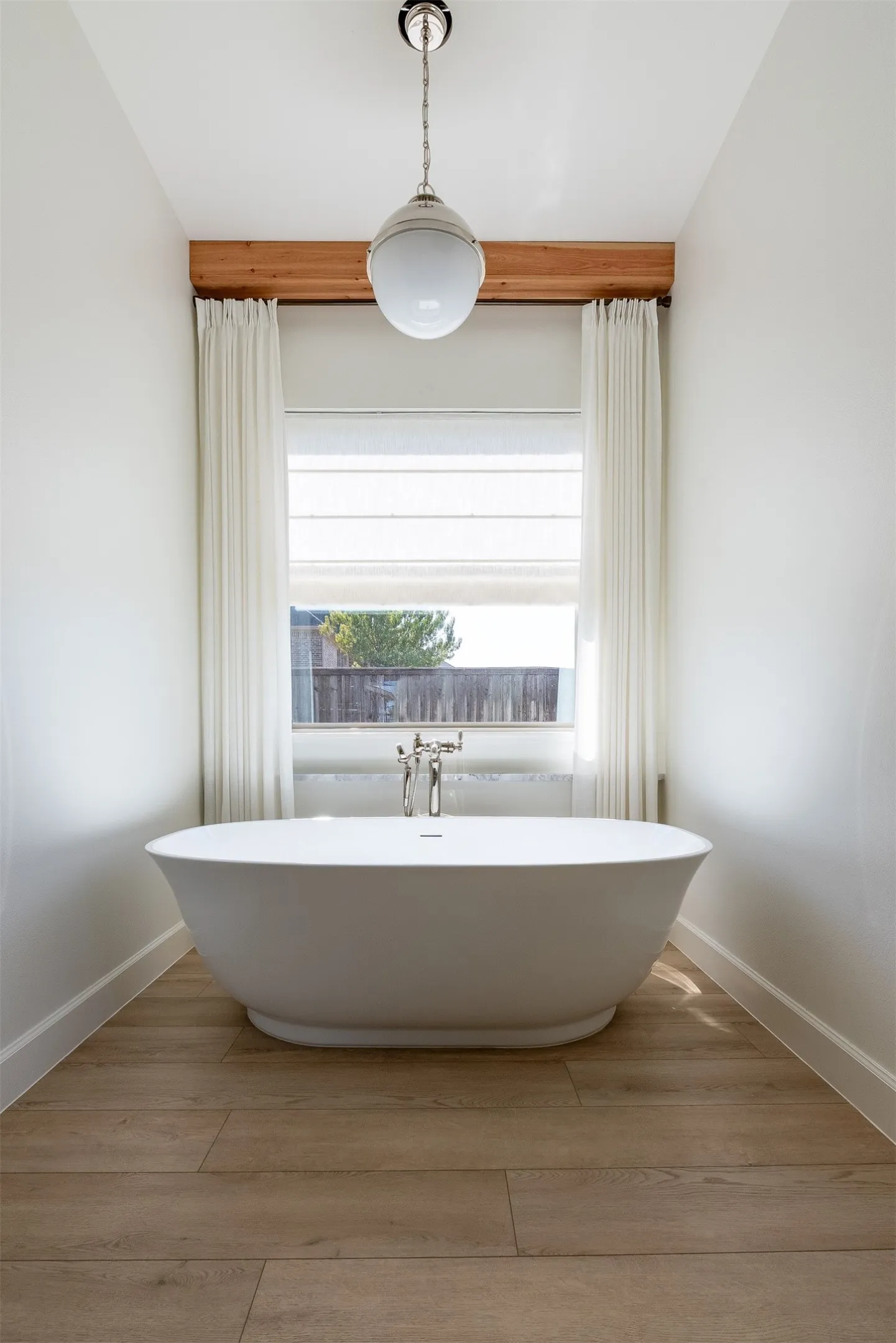 Freestanding soaking tub with chrome fixtures, wood-finish flooring, and a pendant light fixture