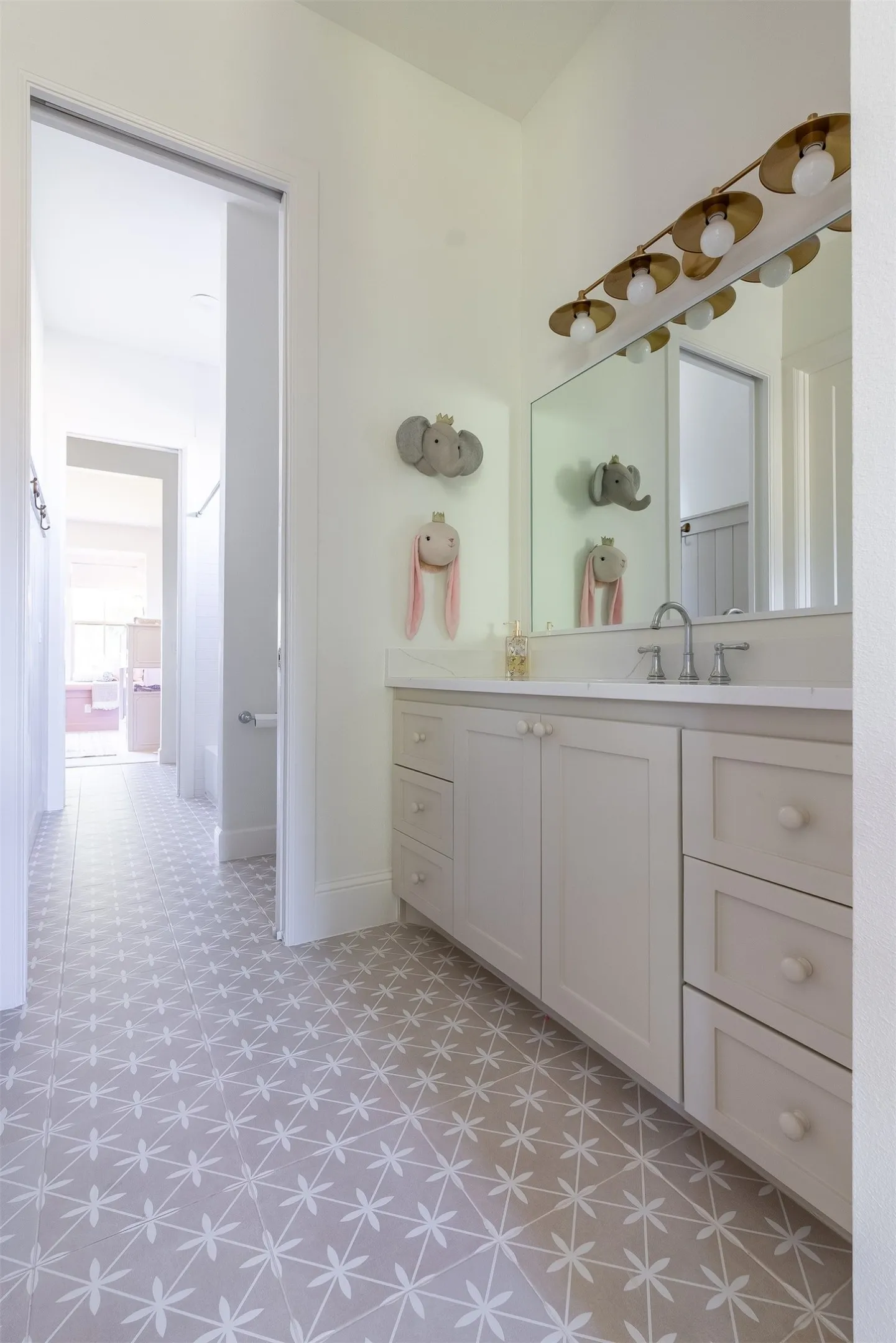 Patterned tile flooring, single vanity with light-colored cabinetry, white countertop, integrated sink, and large wall mirror with overhead lighting